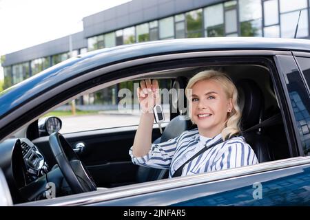 Bonne femme blonde tenant la clé sur le siège conducteur dans la voiture, image de stock Banque D'Images
