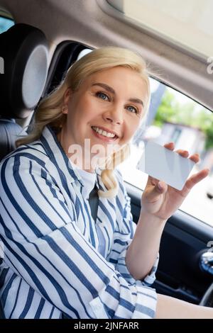 Femme joyeuse tenant un permis de conduire vide dans la voiture, image de stock Banque D'Images