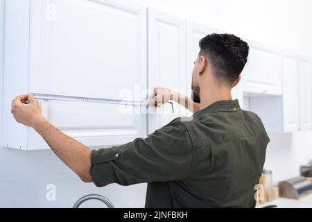 Jeune homme musulman mesurant l'armoire de cuisine à la maison, image de stock Banque D'Images