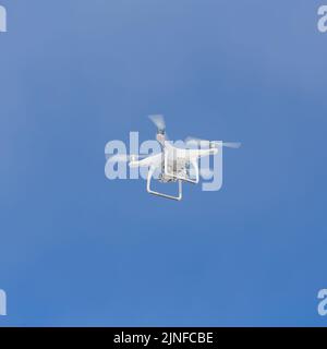 Un drone blanc avec une caméra vidéo et des hélices tournants contre un ciel bleu clair. Banque D'Images