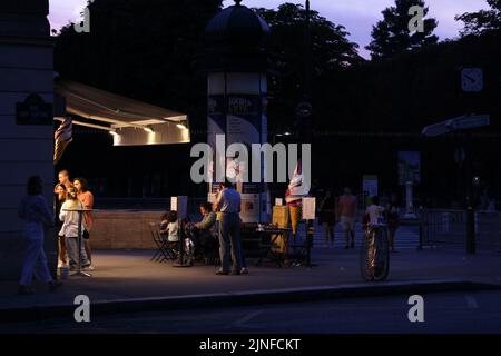 Paris, France - 23 juillet 2022: Les gens commandent et dégusterent des glaces à l'extérieur d'un salon de glace au crépuscule à Paris. Banque D'Images