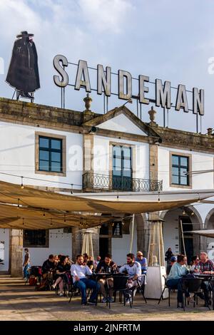 Touristes au café devant les caves à vin et de port de Sandeman sur le front de mer à Vila Nova de Gaia dans le centre de Porto une ville dans le nord du Portugal. Banque D'Images