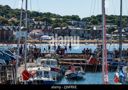 North Berwick, East Lothian, Écosse, Royaume-Uni, 11th août 2022. Météo au Royaume-Uni : rester au frais dans la chaleur. Avec une température atteignant 27 degrés, la ville balnéaire offre des possibilités de se rafraîchir. Les enfants qui se tiennent sur le mur du port sautent dans la mer pendant la vague de chaleur estivale Banque D'Images