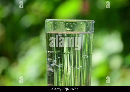 Buvez de l'eau qui coule dans le verre à l'extérieur sur fond de lumière du soleil et de vert naturel sur table blanche Banque D'Images