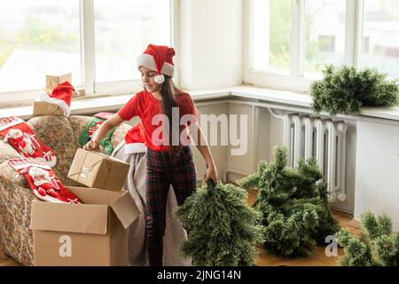 Photo de petite fille gaie mignonne fait un arbre de Noël artificiel porter chapeau de santa à l'intérieur Banque D'Images