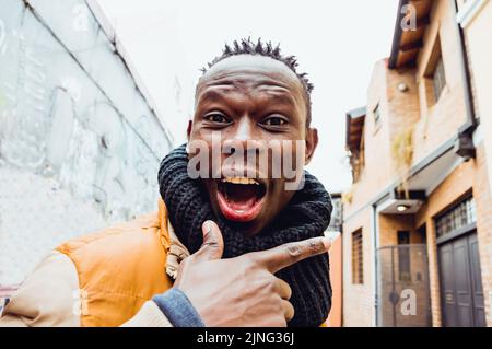 gros plan du jeune africain debout dans la rue, avec un foulard noir, expression de joie et un grand sourire regardant la caméra. Banque D'Images