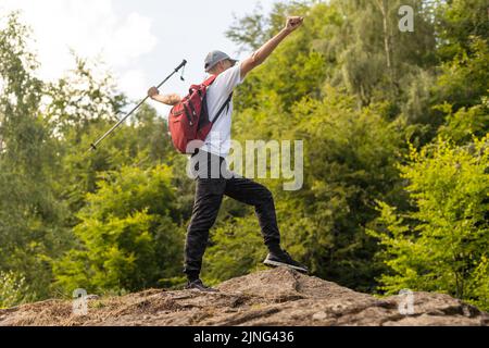 Jeune randonneur avec sac à dos et bâtons de randonnée debout sur le bord de la falaise et regardant les montagnes en été en plein air. Banque D'Images