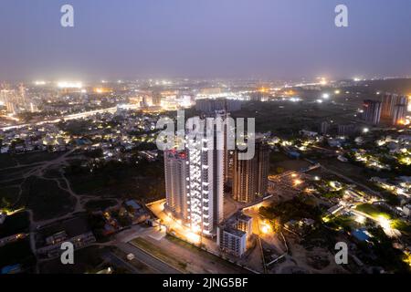 un tir de drone aérien au crépuscule montrant des lumières orange de rues, de maisons et de marchés entourant un gratte-ciel avec le paysage de la ville s'étendant dans le Banque D'Images