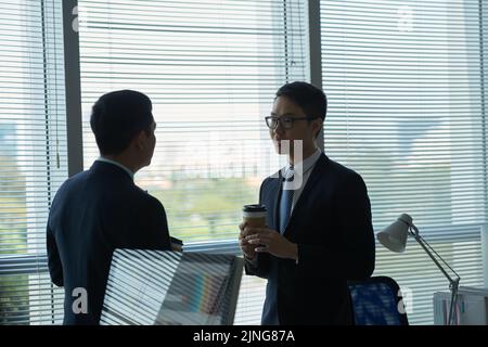 Jeune homme d'affaires vietnamien avec café à emporter en conversation avec un collègue Banque D'Images