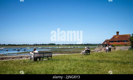 Les gens s'assoient sur des bancs donnant sur Chichester Harbour à Bosham, dans l'ouest du Sussex, au Royaume-Uni. Banque D'Images