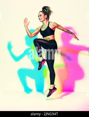 Fille sportive sautant. Photo de femme musclée en noir sportswear sur fond blanc avec effet des ombres de couleurs rvb. Mouvement dynamique. Sports Mo Banque D'Images