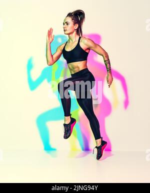 Femme sportive en forme de coureur. Photo de femme musclée en noir sportswear sur fond blanc avec effet des ombres de couleurs rvb. Mouvement dynamique Banque D'Images