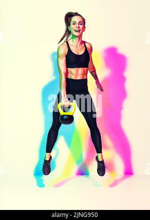 Femme forte sautant avec kettlebell. Photo d'une femme sportive en noir sportswear sur fond blanc avec effet des ombres de couleurs rvb. Force et Mo Banque D'Images