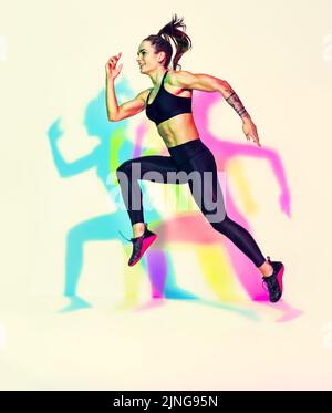 Femme sportive en forme de coureur. Photo de femme musclée en noir sportswear sur fond blanc avec effet des ombres de couleurs rvb. Mouvement dynamique Banque D'Images