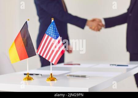 De petits drapeaux de l'Allemagne et des États-Unis se tiennent sur la table au milieu de la poignée de main de deux politiciens. Banque D'Images