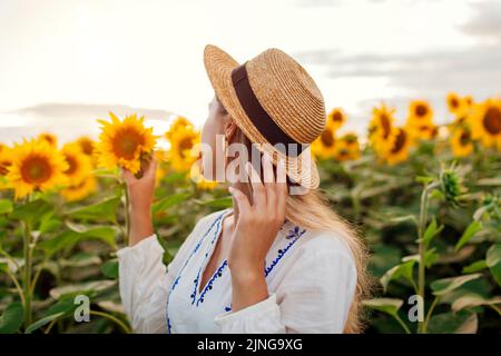 Gros plan de la jeune femme heureuse marchant dans un champ de tournesol en fleurs au coucher du soleil touchant des fleurs. Été en Ukraine. Détente en plein air Banque D'Images