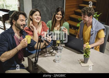 Groupe de jeunes vlogger influenceur amis assis autour de la table streaming en ligne en créant du contenu vidéo pour le vlog en ligne avec interview ou radio Banque D'Images