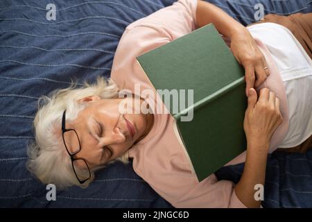 femme âgée couchée sur un canapé et dormant avec un livre Banque D'Images