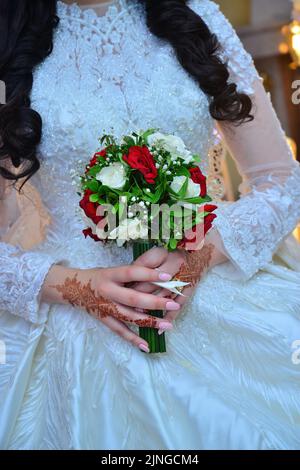 Une mariée arabe tenant un bouquet de mariage avec des tatouages de henné sur ses mains. Concept de mariage islamique Banque D'Images