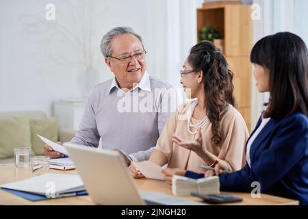 Couple asiatique âgé assis à une table en bois et choisissant un nouvel appartement avec l'aide d'un agent immobilier, intérieur d'un bureau confortable sur fond Banque D'Images