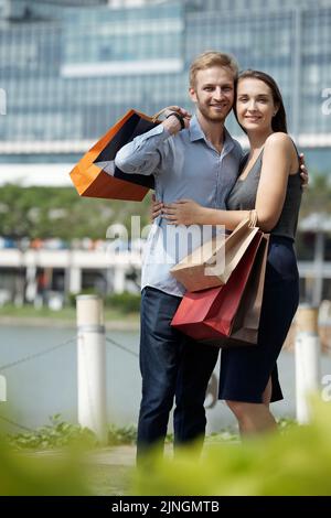 Portrait d'un couple heureux aimant posant avec des sacs de shopping à l'extérieur Banque D'Images