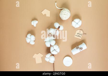 Branche de coton et produits en coton sur fond beige. Vêtements, serviettes, tampons et bâtonnets de coton, fils. Le concept d'écologie et de consum conscient Banque D'Images