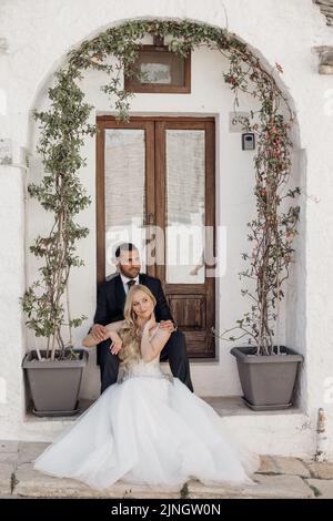 Portrait d'un couple attrayant assis sur la vieille rue près de la porte en bois sous l'arche faite d'arbres entrelacés dans des pots. Banque D'Images