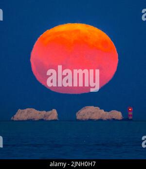 Mudeford, Dorset, Royaume-Uni. 11th août 2022. Météo Royaume-Uni. La pleine superlune de l'Esturgeon s'élève dans le ciel clair de nuit depuis l'arrière du phare des aiguilles sur l'île de Wight au crépuscule à la fin d'une journée chaude brûlante. Crédit photo : Graham Hunt/Alamy Live News Banque D'Images