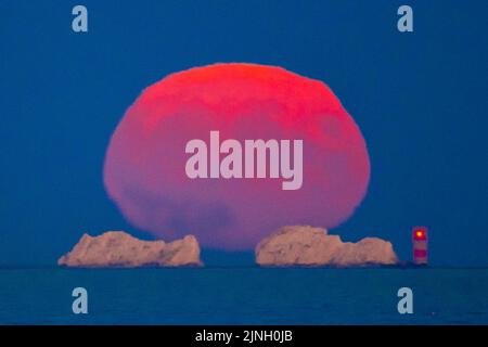 Mudeford, Dorset, Royaume-Uni. 11th août 2022. Météo Royaume-Uni. La pleine superlune de l'Esturgeon s'élève dans le ciel clair de nuit depuis l'arrière du phare des aiguilles sur l'île de Wight au crépuscule à la fin d'une journée chaude brûlante. Crédit photo : Graham Hunt/Alamy Live News Banque D'Images