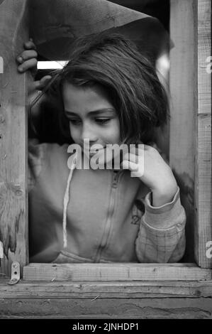 Photo verticale en niveaux de gris d'une petite fille de réfugiés souriante dans un camp d'Ersal, au Liban Banque D'Images