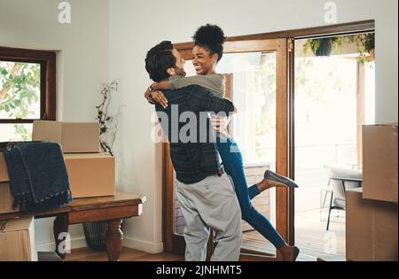 Couple de propriétaires célébrant, embrassant et encourageant dans la nouvelle maison en tant qu'investisseurs immobiliers, acheteurs et propriétaires. Amusant interracial homme et femme à la recherche Banque D'Images