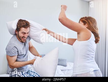 OK je rends. Un couple ayant un combat d'oreiller à la maison. Banque D'Images