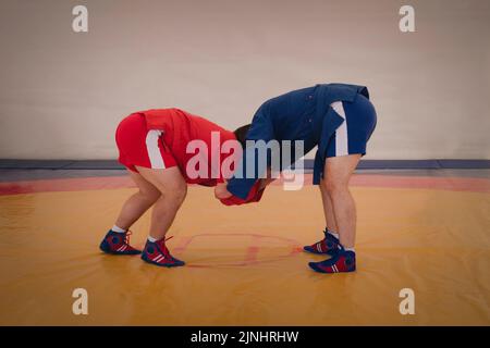 deux hommes en bleu et rouge se battent sur un tatami jaune. Les lutteurs de Sambo s'entraînent. Concours Sambo dans le hall. Banque D'Images