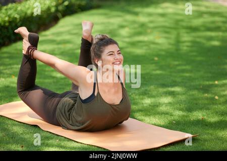 Jeune femme gaie portant un haut et des leggings faisant de l'exercice d'étirement tout en appréciant l'air frais dans le parc public vert Banque D'Images