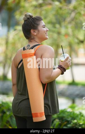 Une jeune femme attrayante portant des leggings et un haut qui profite de la beauté du parc d'été et de la boisson fouettée de la tasse en plastique après un entraînement en plein air productif Banque D'Images