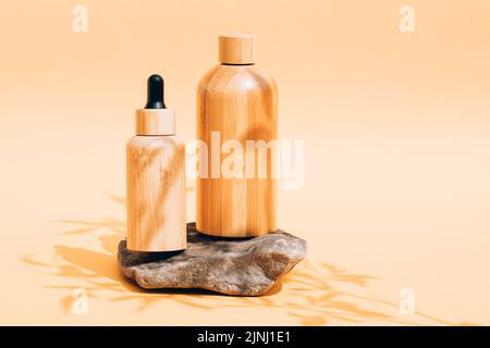 Bouteilles en bois avec produits de soin organique de la peau sous la lumière du soleil avec des ombres de feuilles. Soins de beauté naturels sur fond jaune clair W Banque D'Images