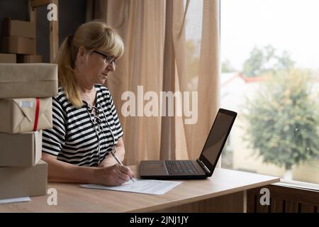 Vendeur en ligne femme plus ancienne dactylographie clavier d'ordinateur portable vérifier commande en ligne, vérifier les marchandises livraison paquet expédition postale. Jeune femme mature démarrage petit Banque D'Images