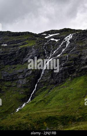 Plan vertical d'une chute d'eau tombant sur les rochers mousseux sous un ciel gris nuageux Banque D'Images