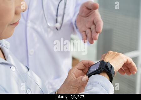 Gros plan d'un patient méconnaissable qui vérifie sa fréquence cardiaque à l'aide d'une montre intelligente tout en consultant un médecin Banque D'Images