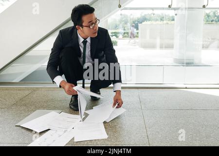 Un homme d'affaires asiatique effrayé se ramassant des documents tombés sur le sol Banque D'Images