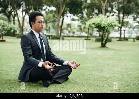 Jeune homme d'affaires asiatique en costume pratiquant la méditation en plein air dans le parc Banque D'Images