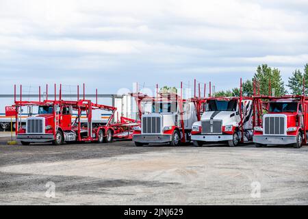 Grands rigs industriels standard rouge vif et blanc transporteurs semi-remorques avec semi-remorques hydrauliques modulaires vides se trouvant sur l'aire de stationnement Waiti Banque D'Images