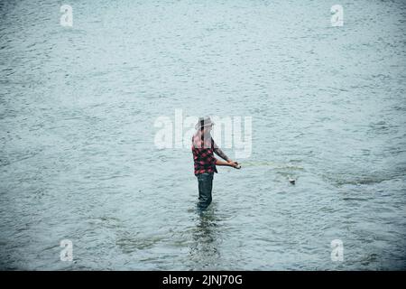 Fisher homme dans l'eau attrapant le poisson, vue de dessus. Pêcheur avec tige, tambour tournant sur la rive de la rivière. Homme attrapant le poisson, tirant la tige tout en pêchant sur le lac. Banque D'Images