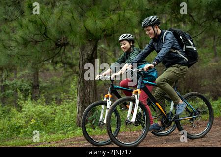 Vue latérale d'un jeune couple asiatique portant un casque tout en pratiquant le vélo de fond Banque D'Images