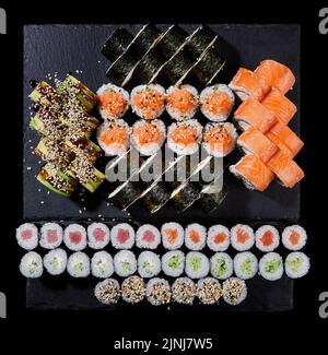 Petits pains à sushis de cuisine japonaise sur un panneau en pierre. Différents types de rouleaux de sushi avec différents poissons, légumes, fromage, sésame et avocat sur un g Banque D'Images