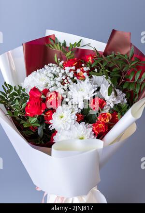 Arrangements floraux. Gros plan de fleurs blanches et rouges enveloppées de papier floral brillant sur fond bleu. Bouquet de roses roses, chrysanthèmes blancs, Banque D'Images