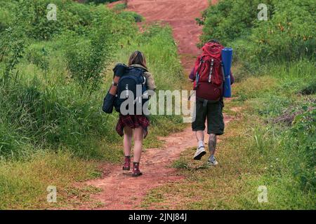 Vue arrière des jeunes randonneurs avec des sacs à dos s'amuser tout en marchant le long du chemin dans la zone brousse Banque D'Images