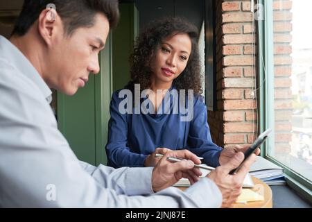 Un groupe de responsables asiatiques se sont réunis dans le hall d'entrée du bureau pour réfléchir à un projet ambitieux, un homme d'âge moyen utilisant une tablette numérique Banque D'Images