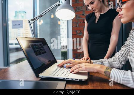 Femme décoratrice d'intérieur travaillant avec un client regardant des photos à l'aide d'un ordinateur portable assis dans un studio moderne. Banque D'Images