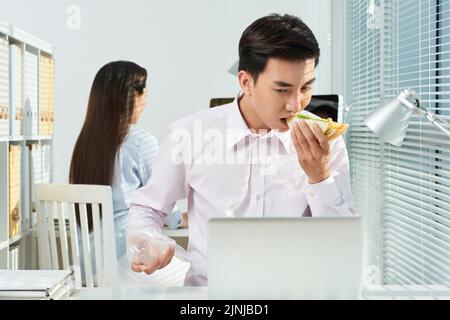 L'homme d'affaires asiatique s'est concentré sur le travail manger sandwich Banque D'Images